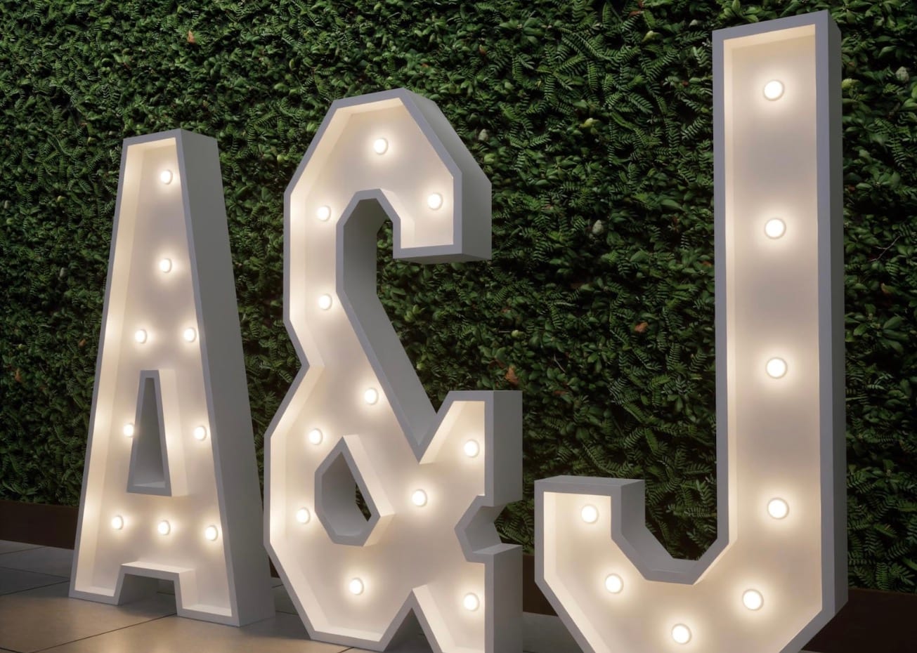 Marquee letters A & J displayed against a greenery wall